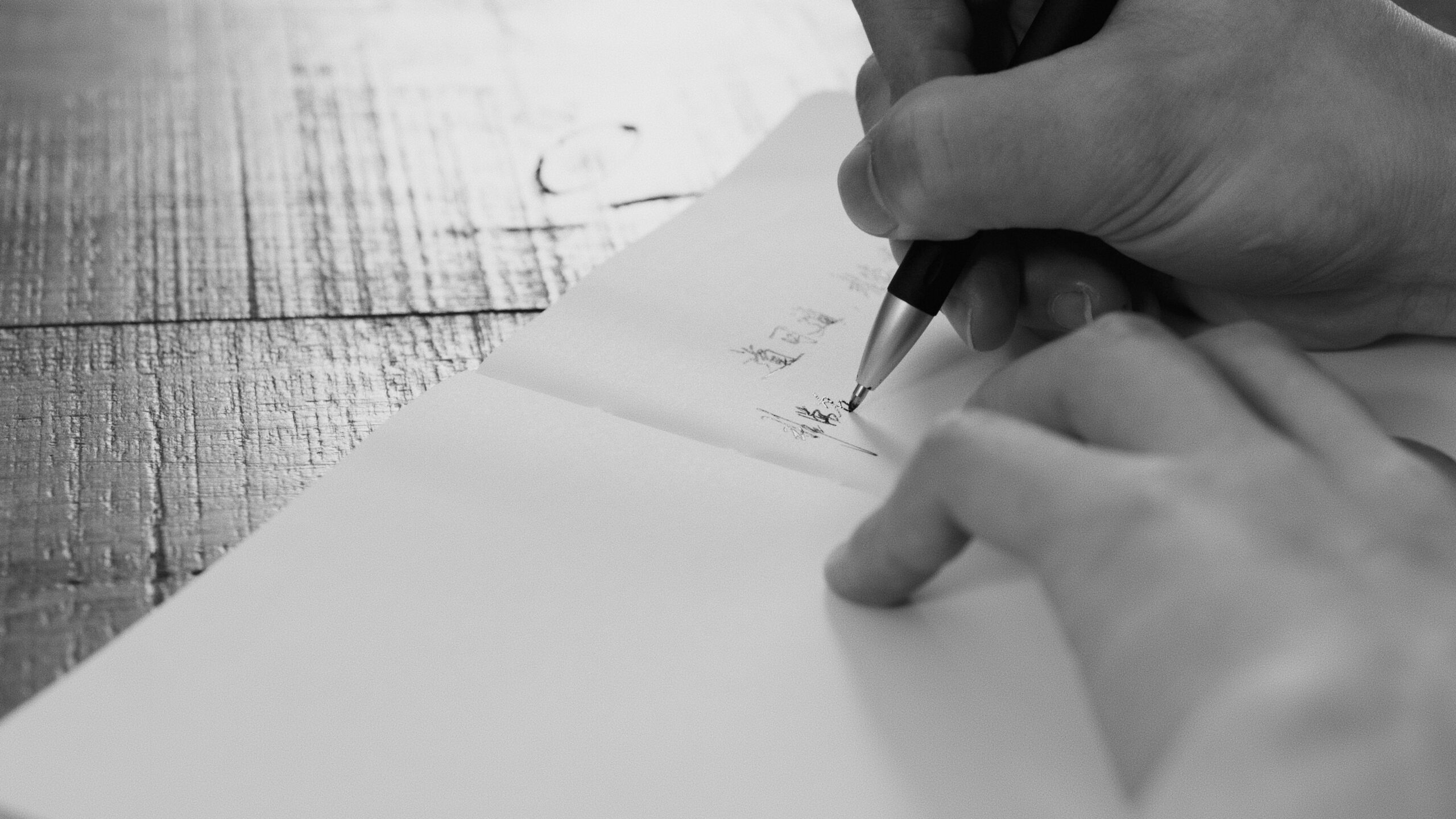 Black and white image showing hands writing with a pen on paper.