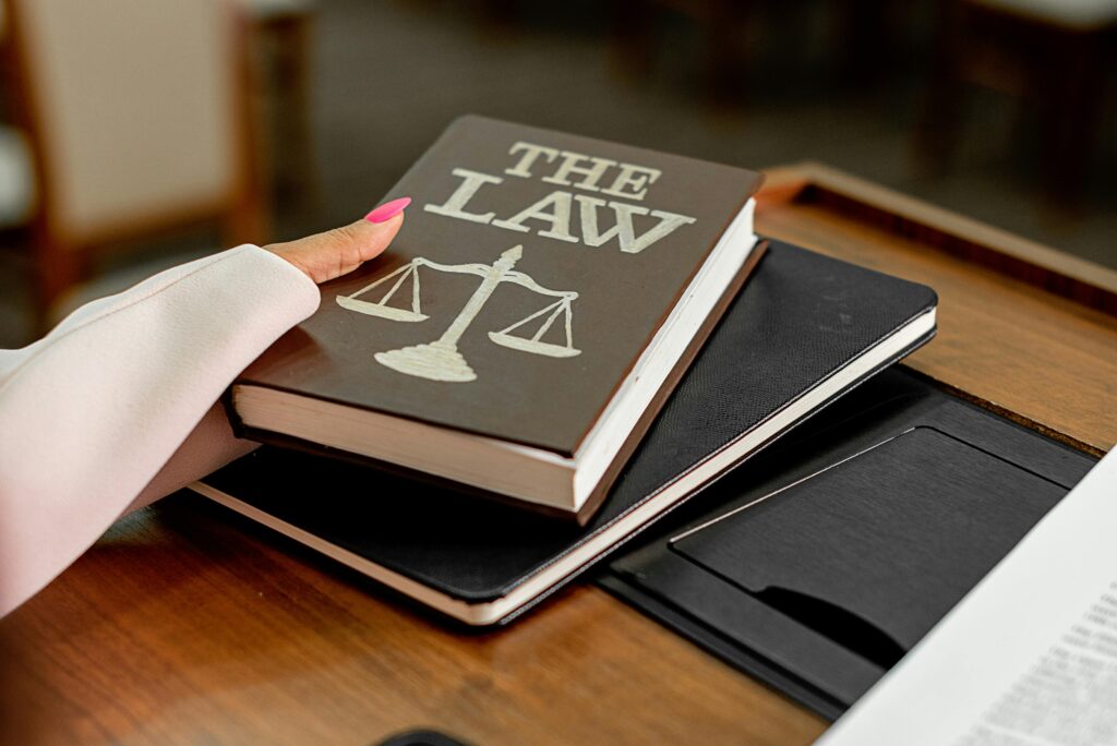 Closeup image of a law book titled 'The Law' on a wooden desk with scales of justice.