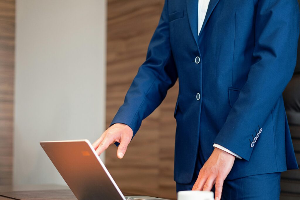 Business professional in a suit using a laptop on a desk in an office setting.